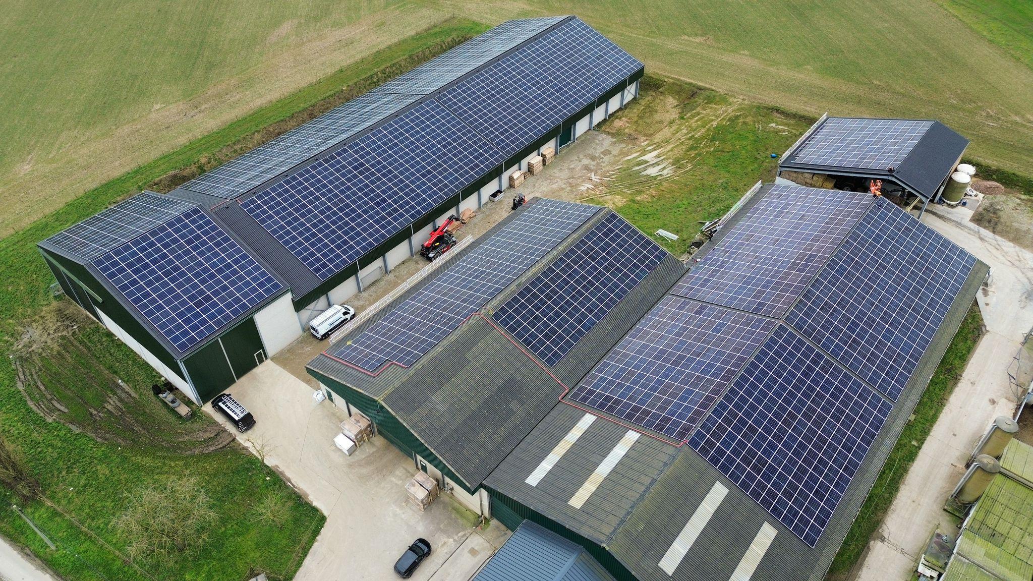 Luchtbeeld van bedrijfsdaken volledig bedekt met zonnepanelen, tussen groene velden
